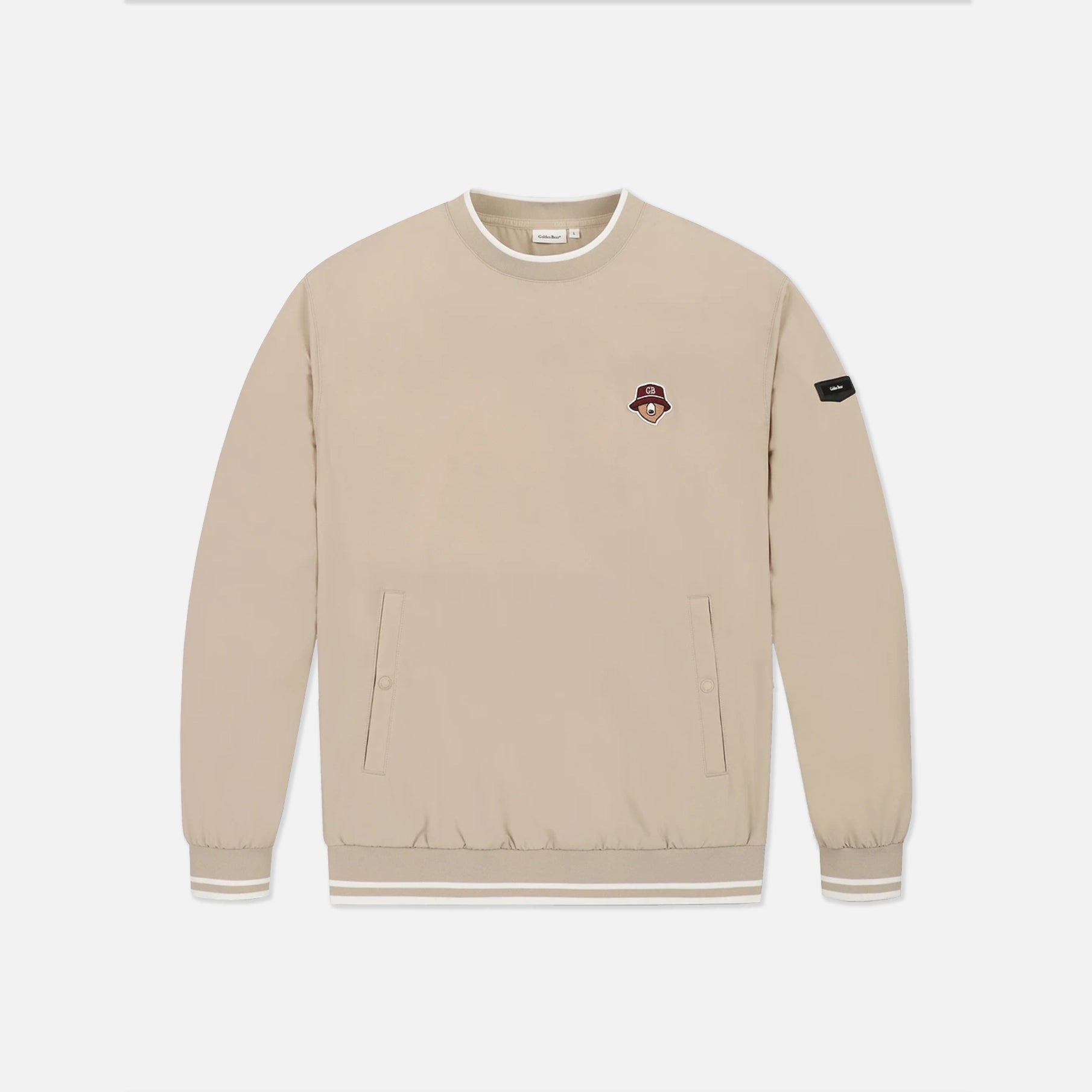 A beige crewneck sweatshirt with a small embroidered character patch on the left chest and a black brand patch on the right sleeve, displayed on a clean white background.
