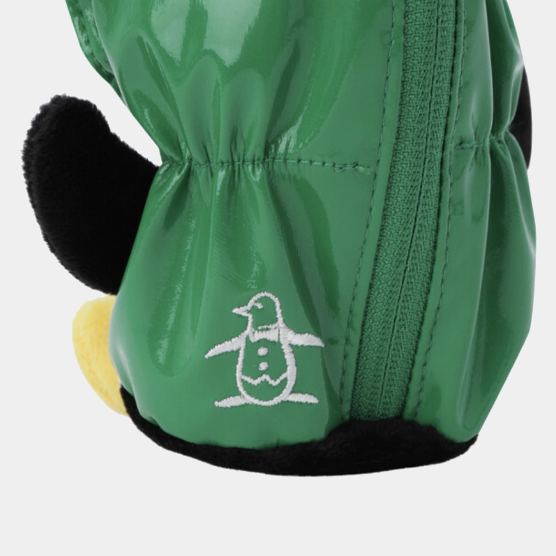 Close-up of a green penguin-themed winter golf ball case with a white embroidered penguin logo, black plush ear, and yellow beak detail on a light gray background.