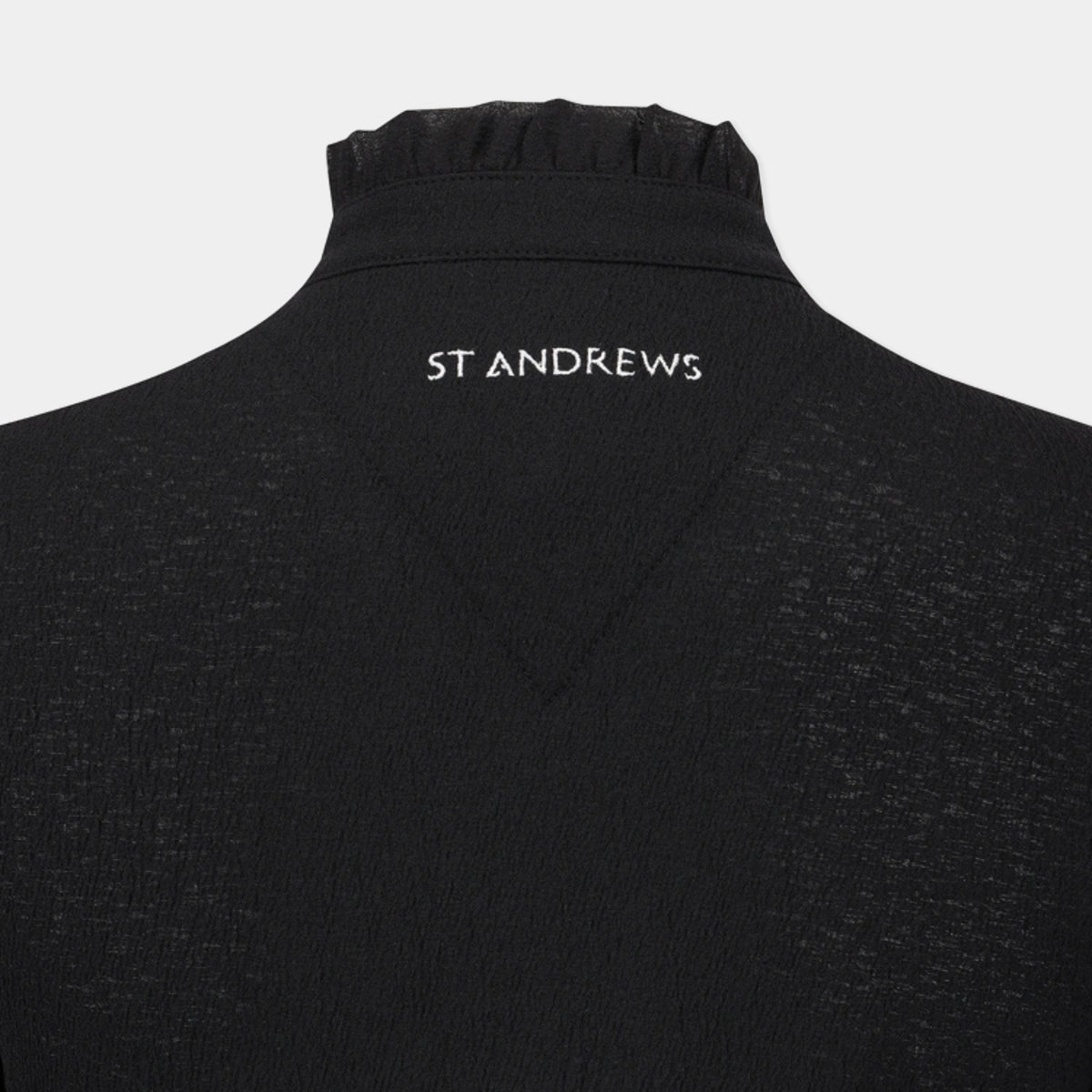Close-up of the back of a black knit top with a high gathered collar and the brand name 'ST ANDREWS' printed in white text at the center of the neck.