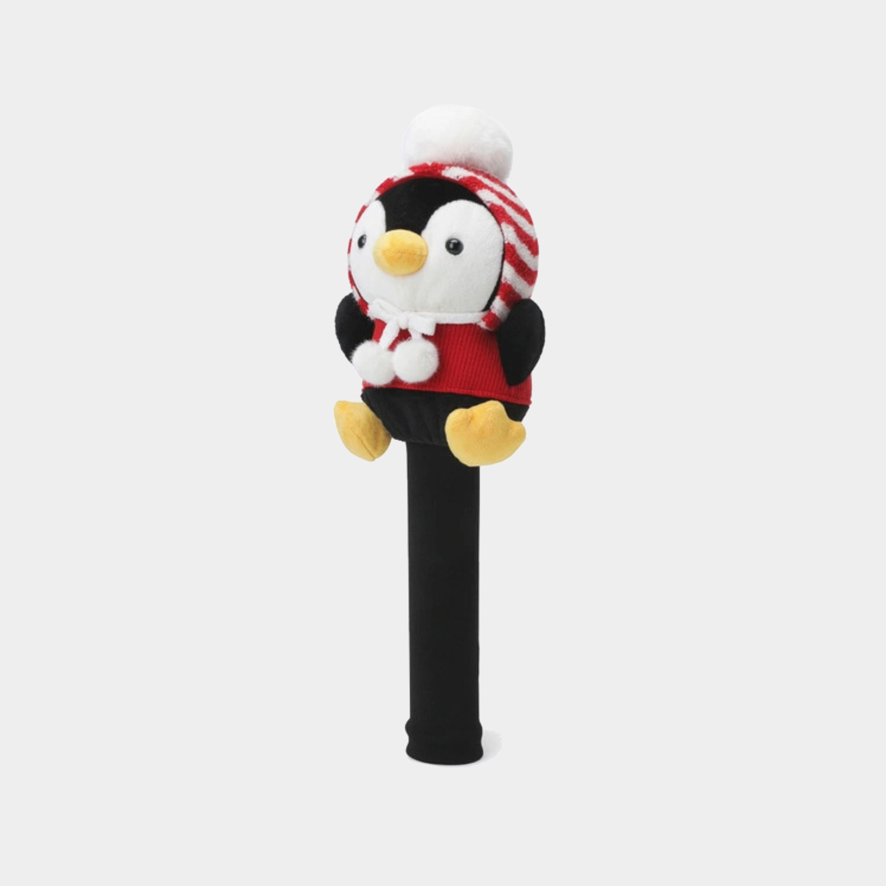 A plush penguin golf club headcover on a black shaft, featuring a white and red striped knit hat with a white pom-pom, a red sweater, and yellow feet, set against a light gray background.