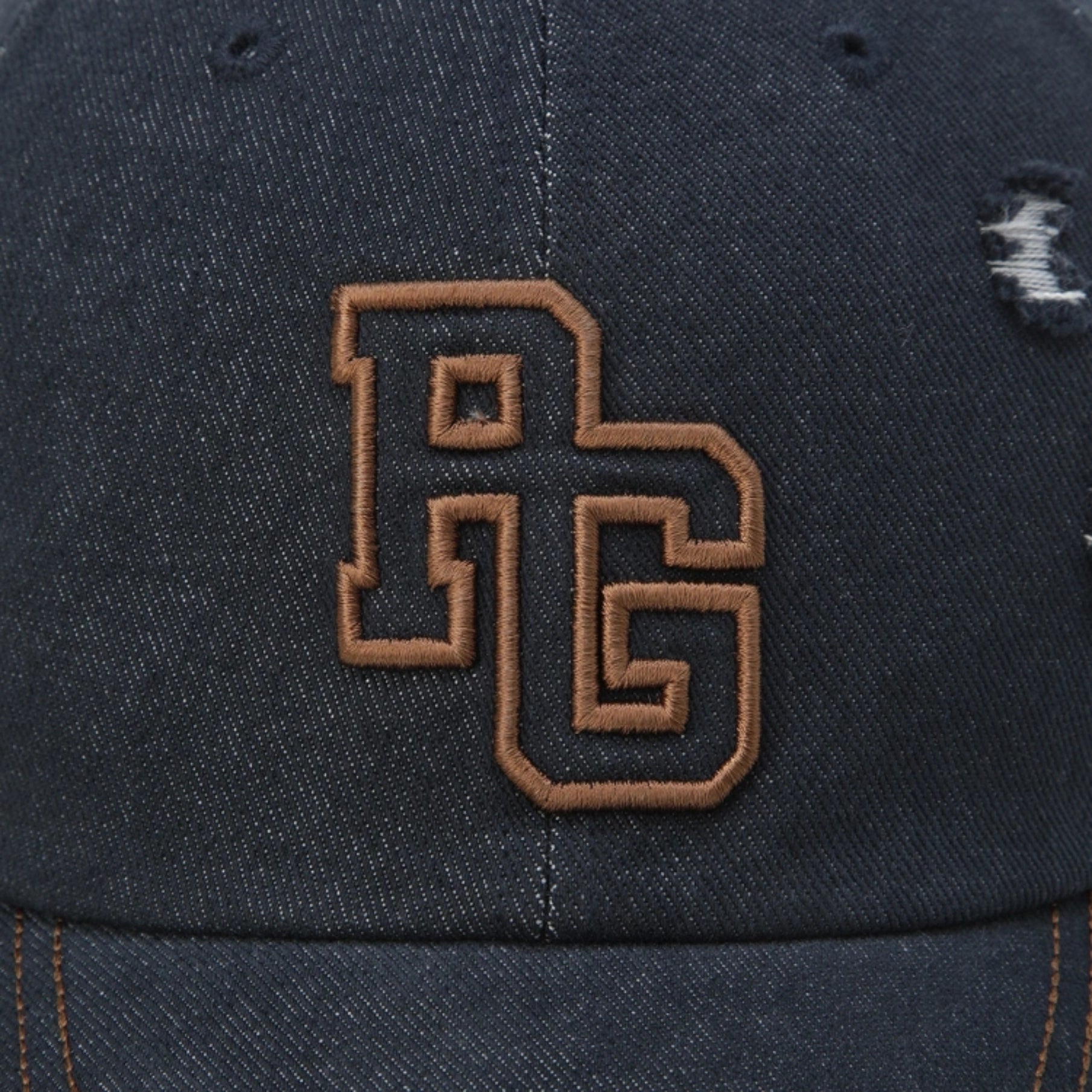 Close-up of a dark navy distressed baseball cap featuring an embroidered brown interlocking 'RG' logo on the front panel.