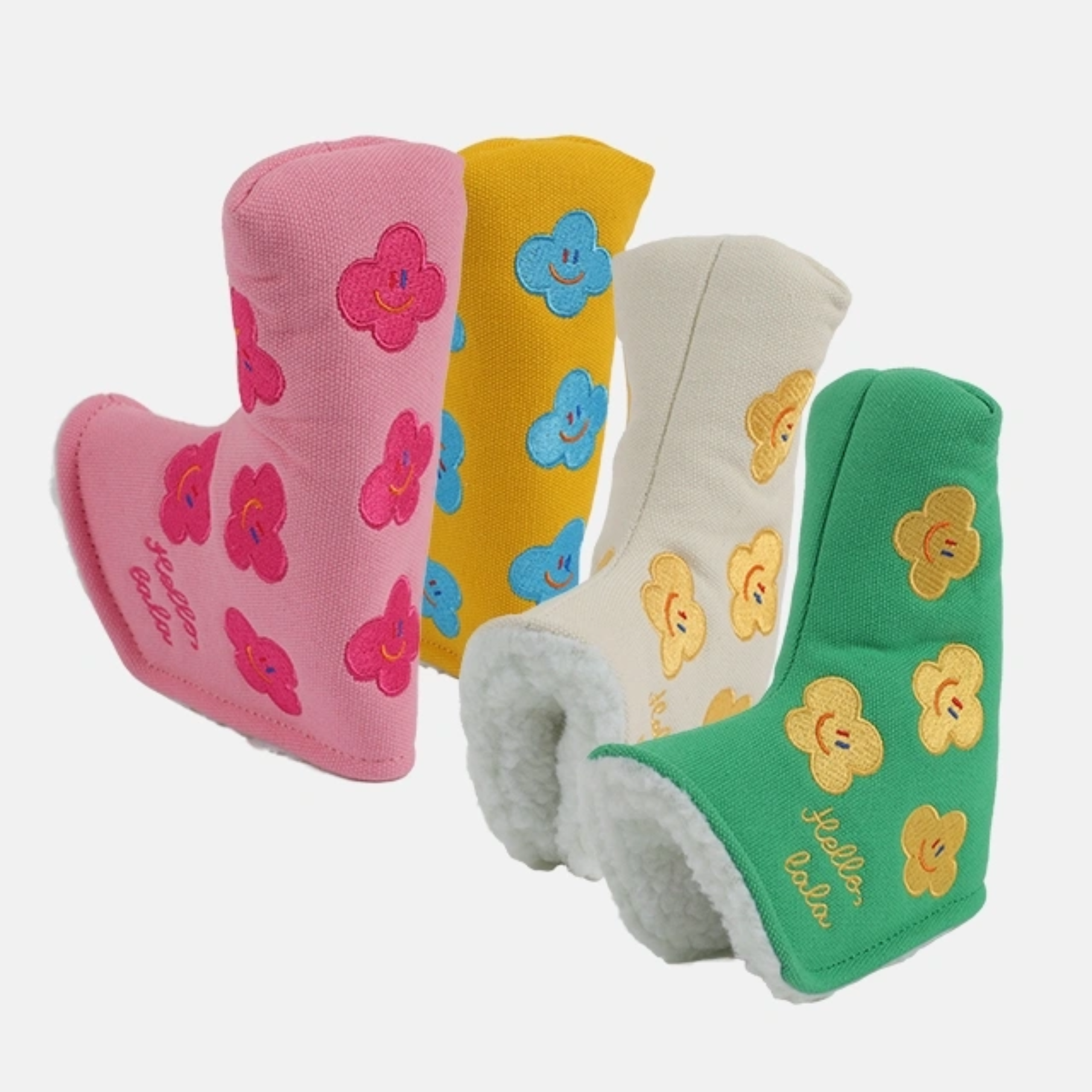 Four plush boot-shaped headcovers in pink, yellow, cream, and green, each decorated with embroidered smiling flowers and white faux-fur trim, shown on a light gray background.