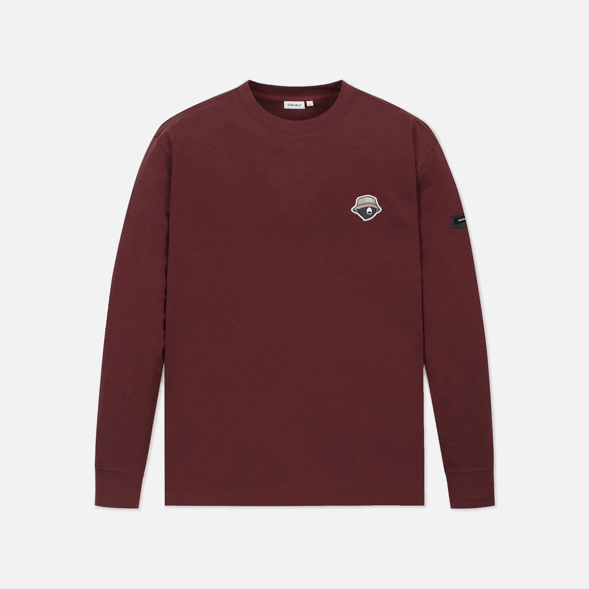 A long-sleeve crewneck shirt in maroon, featuring a small embroidered shield logo on the left chest and a black brand tag on the right sleeve, displayed against a light gray background.