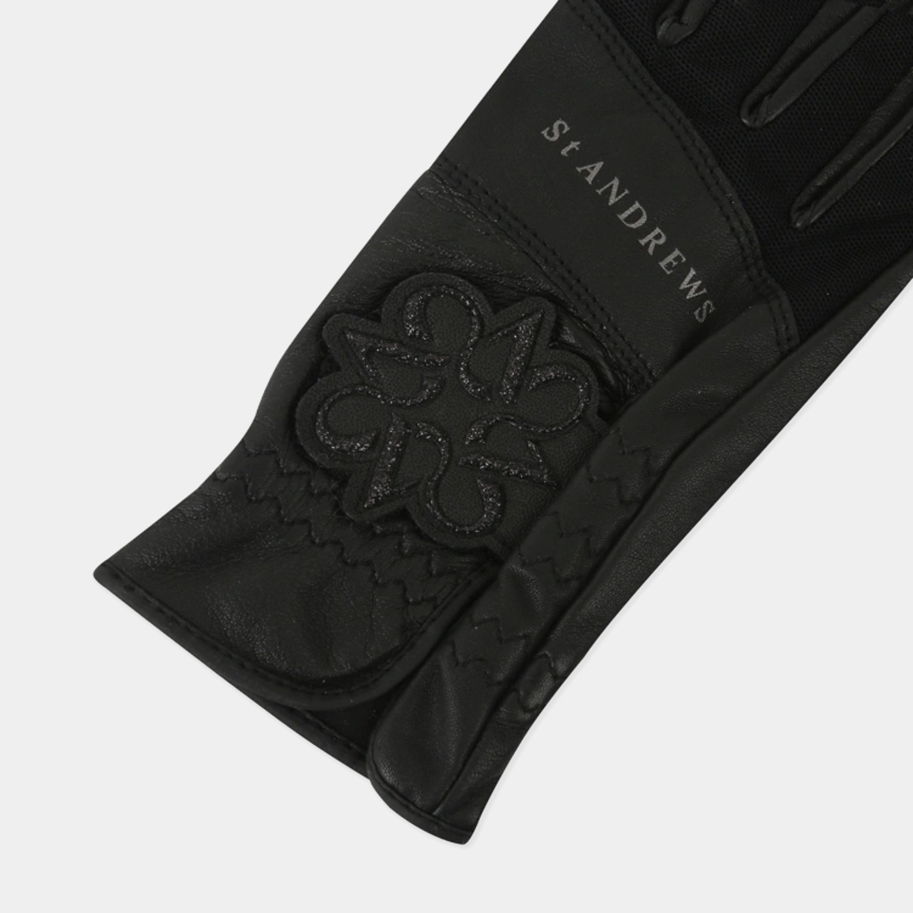 A close-up of a black St. Andrews equestrian glove, showing the textured leather cuff with a debossed brand logo and the brand name 'ST ANDREWS' printed in white on the back of the hand.