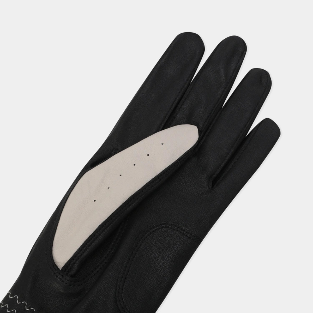 Close-up of the black leather golf glove showing the beige thumb panel and palm details.