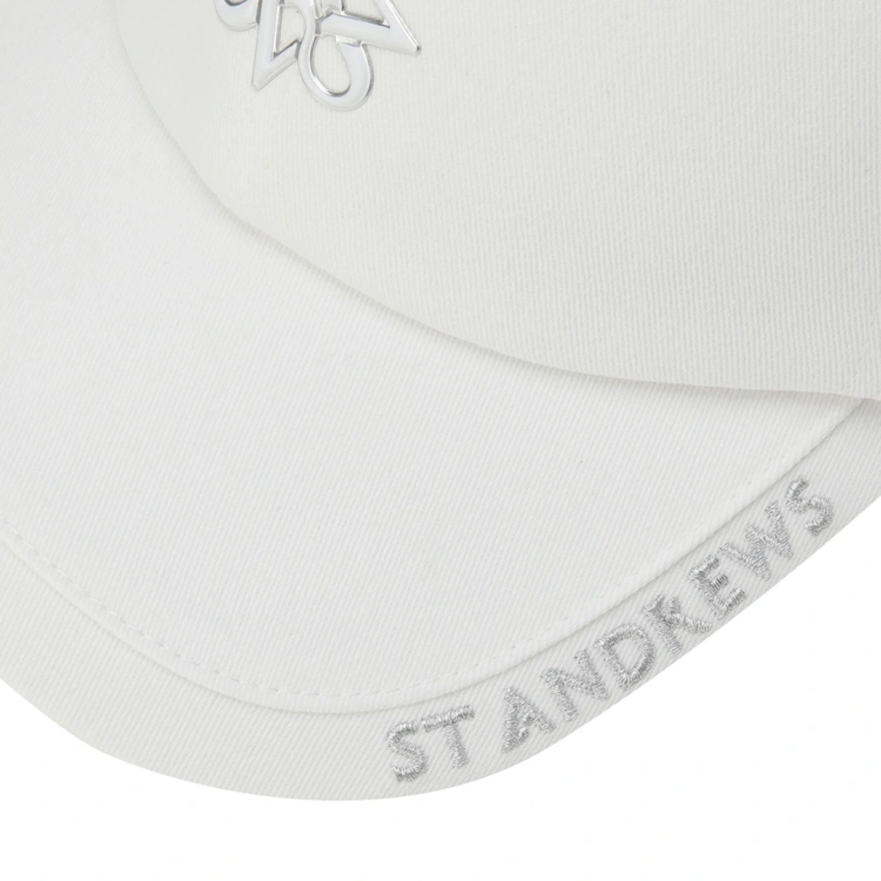 Close-up of a white baseball cap showing the curved brim with 'ST ANDREWS' embroidered in white on the side, and part of a metallic silver logo on the front.