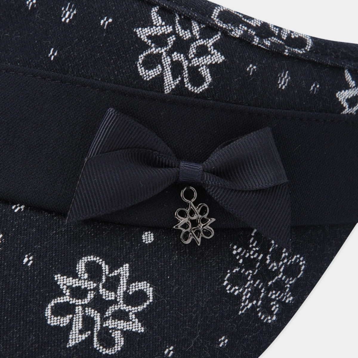 Close-up of a dark navy fabric accessory with a wide band, a large matching bow, and a small silver flower charm, set against a light gray background.