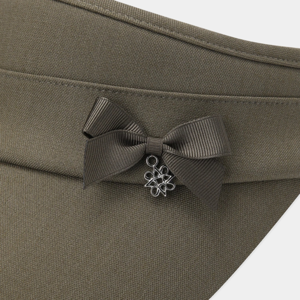 Close-up of an olive green fabric accessory with a dark brown ribbon bow and a small silver metal flower charm.