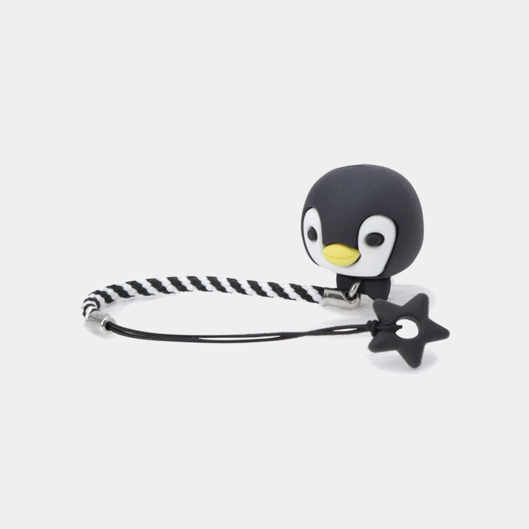 A black and white braided cord bracelet with a 3D penguin charm featuring a yellow beak, and a dangling black star-shaped charm, shown on a light gray background.