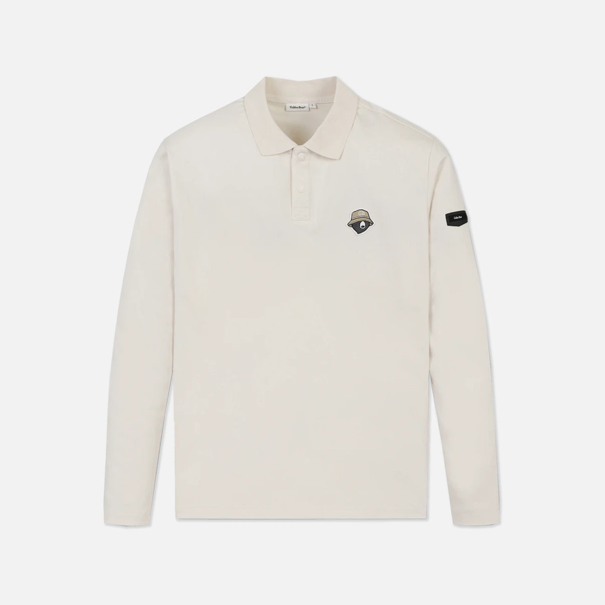 An off-white long-sleeve polo shirt with a small embroidered shield logo on the left chest and a black brand patch on the right sleeve, shown against a light gray background.