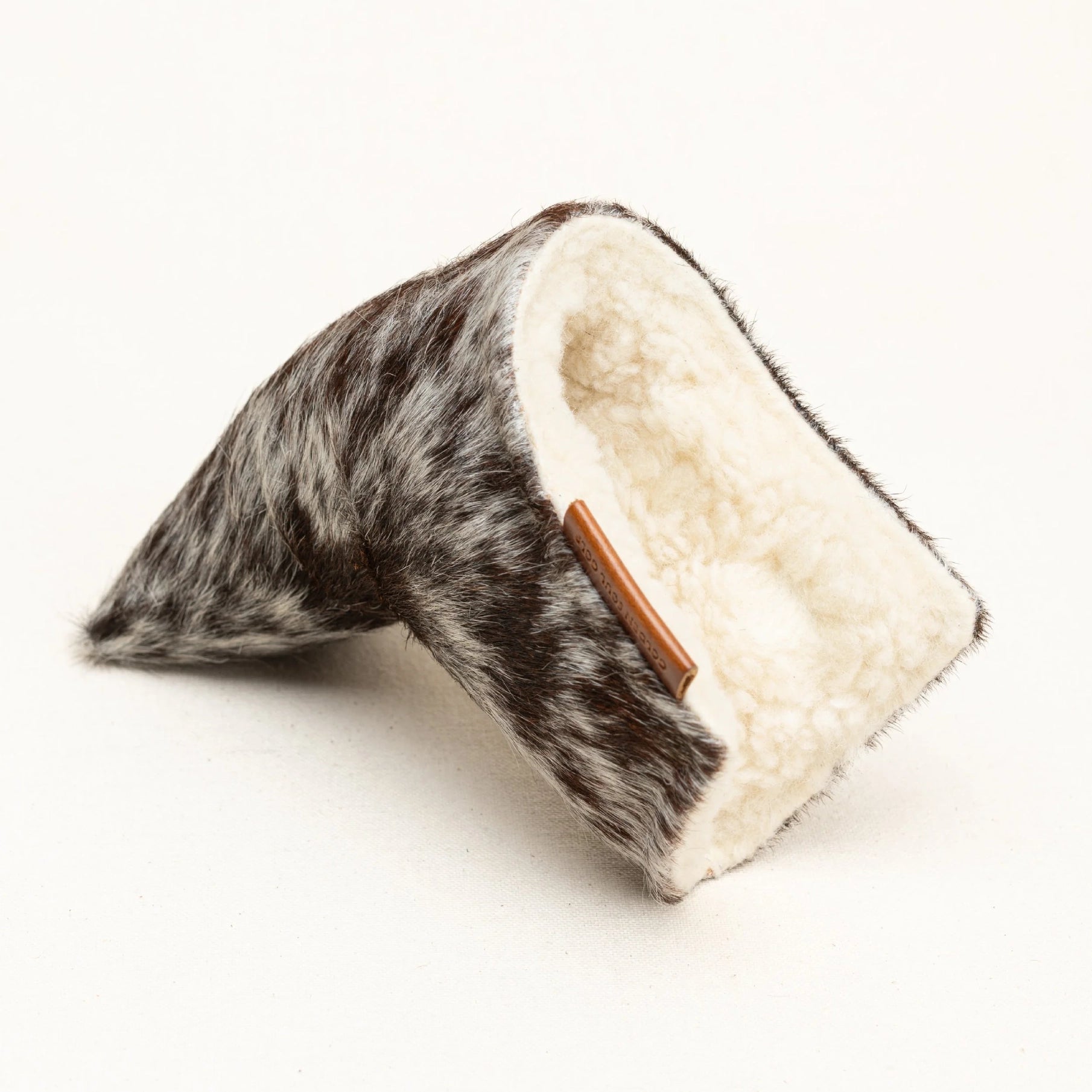A wedge-shaped putter cover featuring a brown and black spotted cowhide exterior and a soft cream fleece interior, with a small brown leather accent on the side, shown on a plain white background.