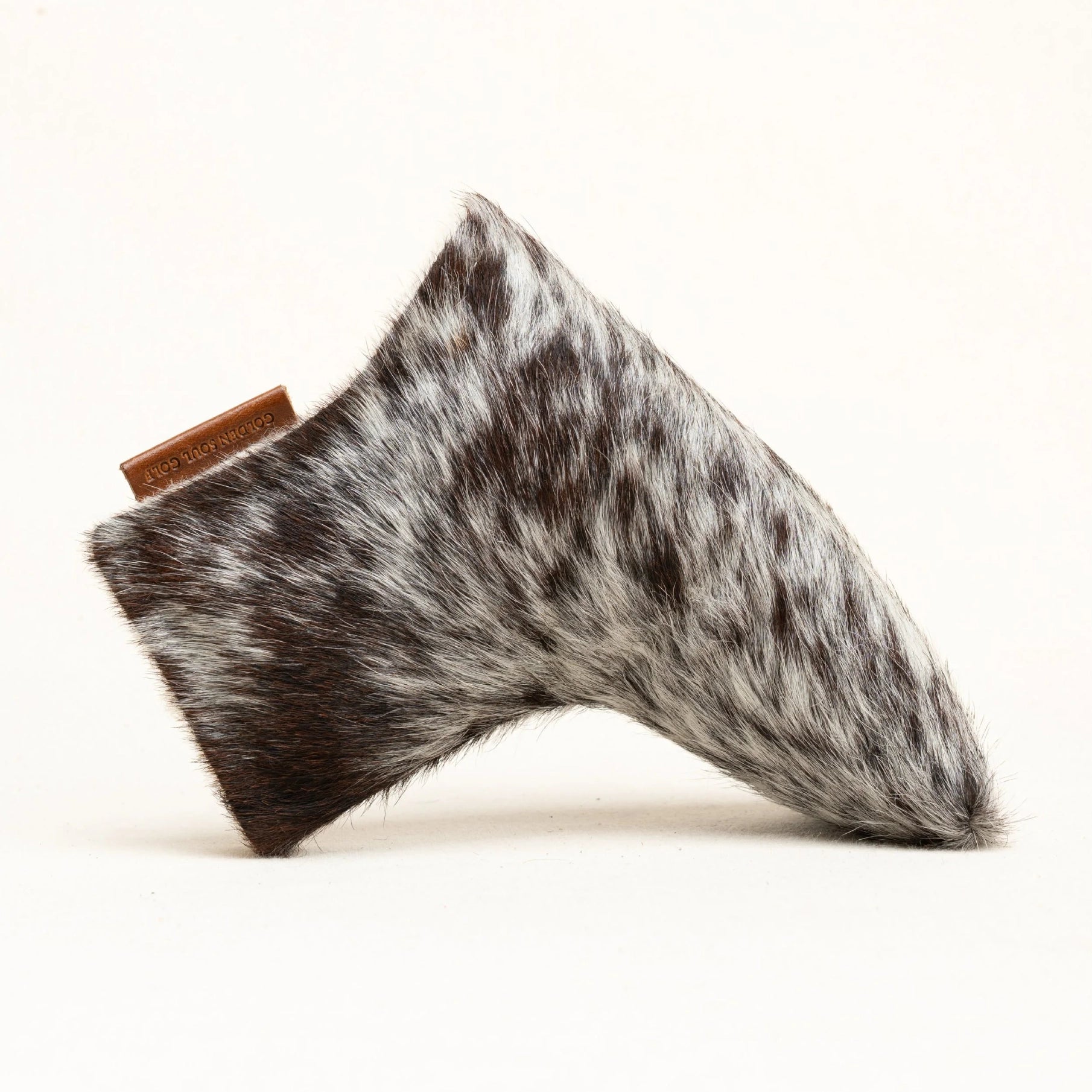 A putter cover made of black and white mottled faux fur, featuring a small brown leather tag on the side, photographed against a clean white background.