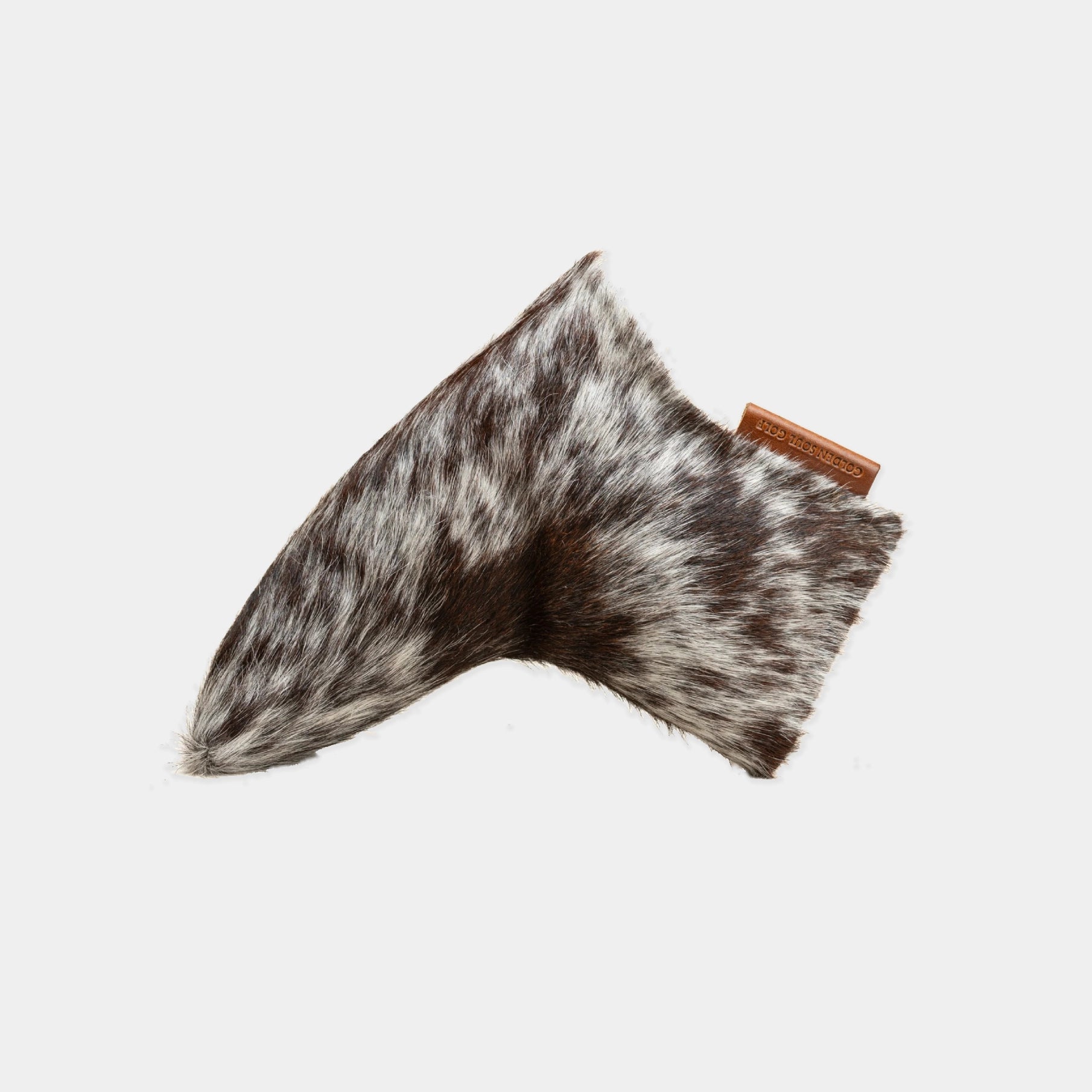 A putter cover made from mottled brown, black, and white animal fur, with a small brown leather tag attached on the right side, shown against a plain light gray background.