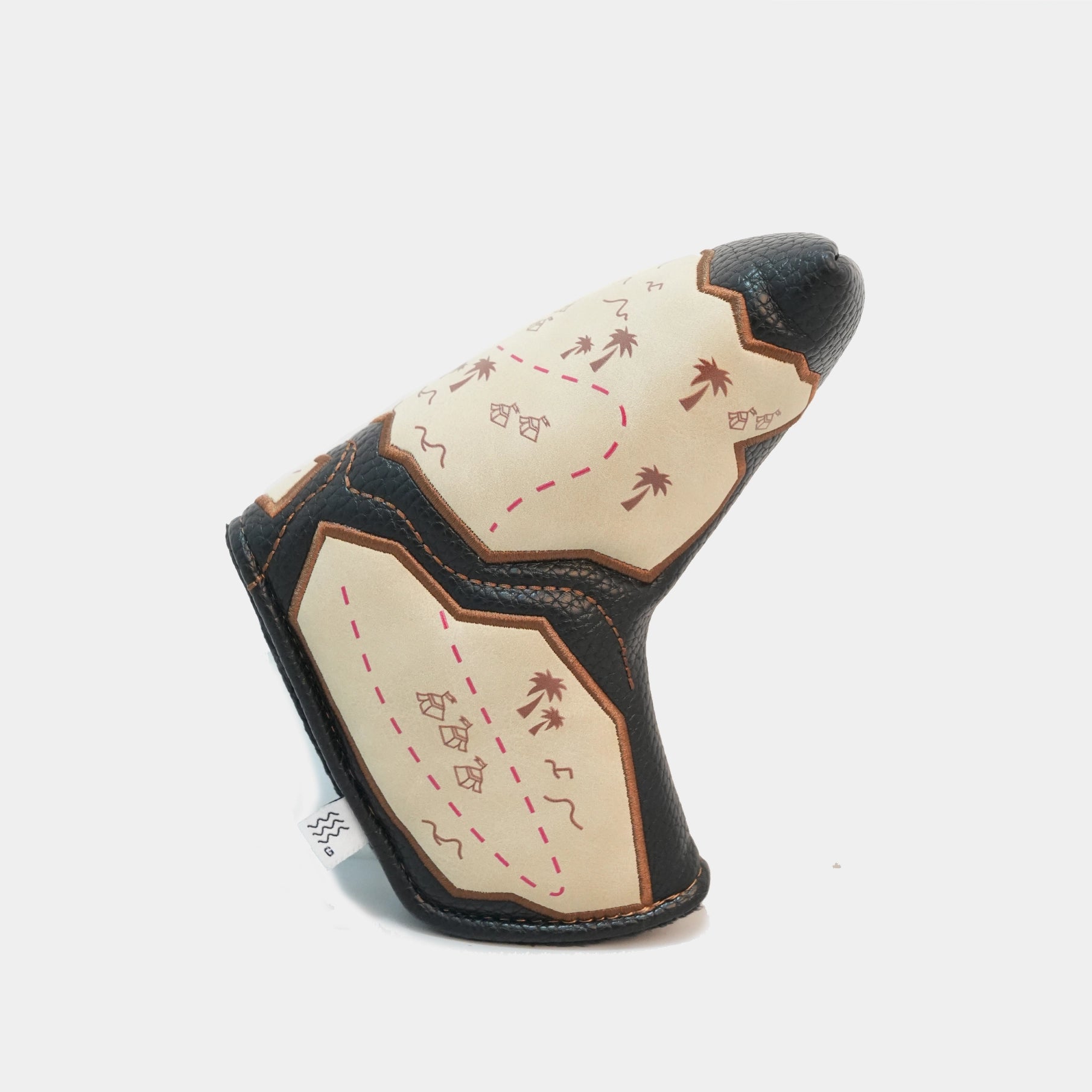 A golf club headcover with a desert map design, featuring cream-colored panels with brown palm trees and red dashed lines, bordered by black leather and brown stitching, on a light gray background.