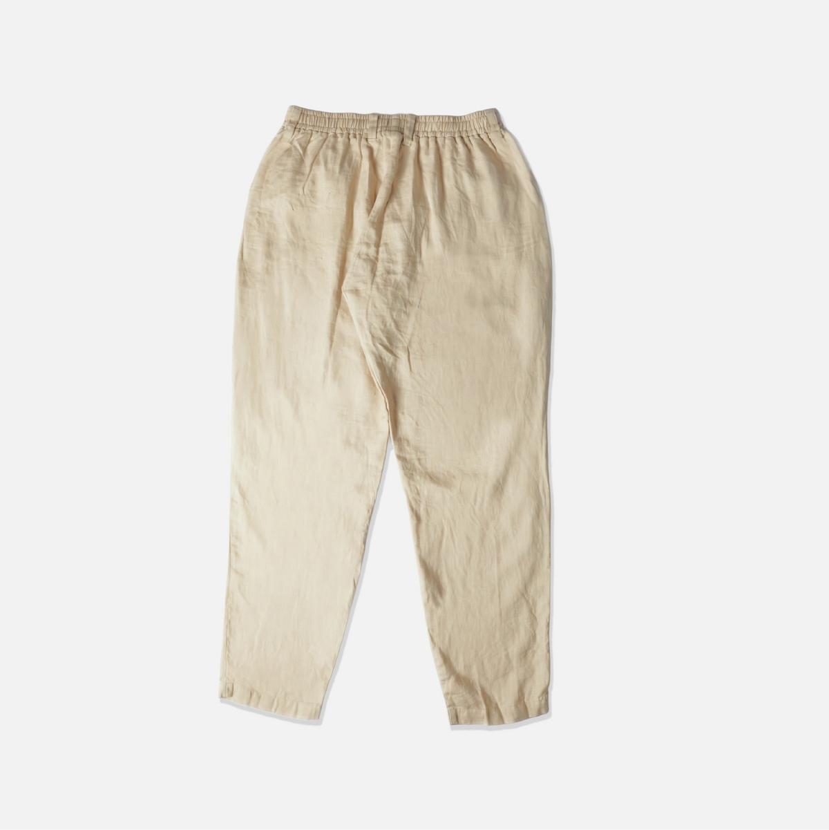A pair of light beige linen pants with an elastic waistband, laid flat against a clean white background.