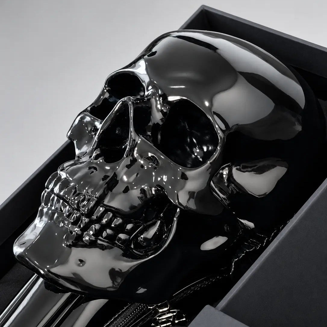 A glossy black skull-shaped object displayed inside a dark presentation box, photographed on a clean light gray background.