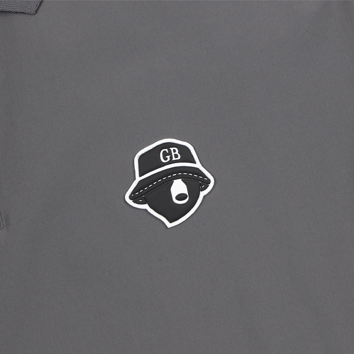 A close-up of a dark gray garment featuring a central graphic sticker or patch of a black bucket hat with white lettering and a white outline.