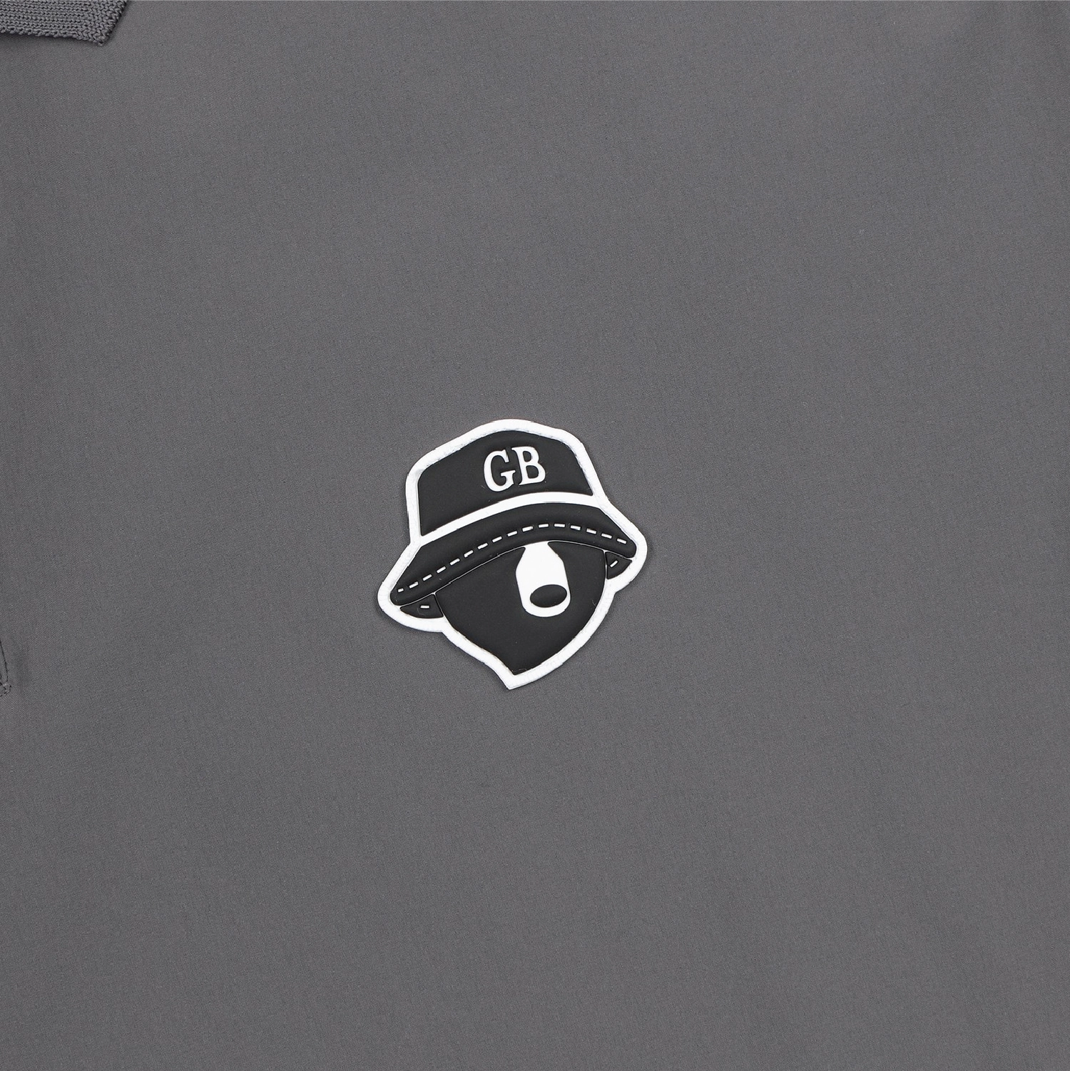A close-up of a dark gray garment featuring a central graphic sticker or patch of a black bucket hat with white lettering and a white outline.
