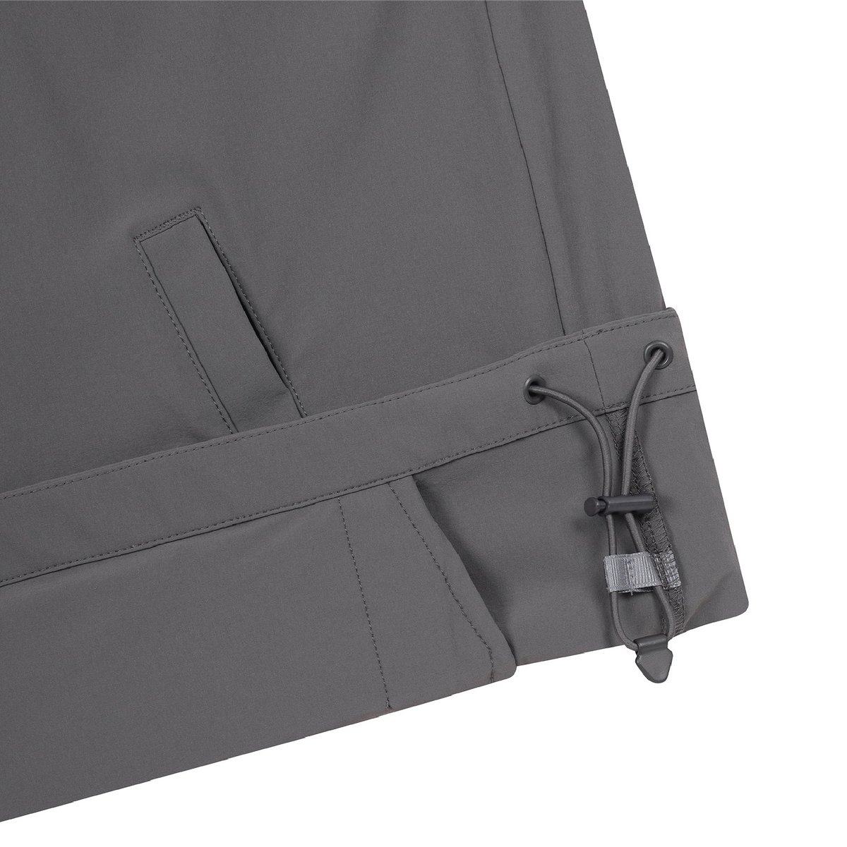 Close-up of the lower corner of dark gray outdoor pants showing a drawstring hem with a toggle closure, on a white background.