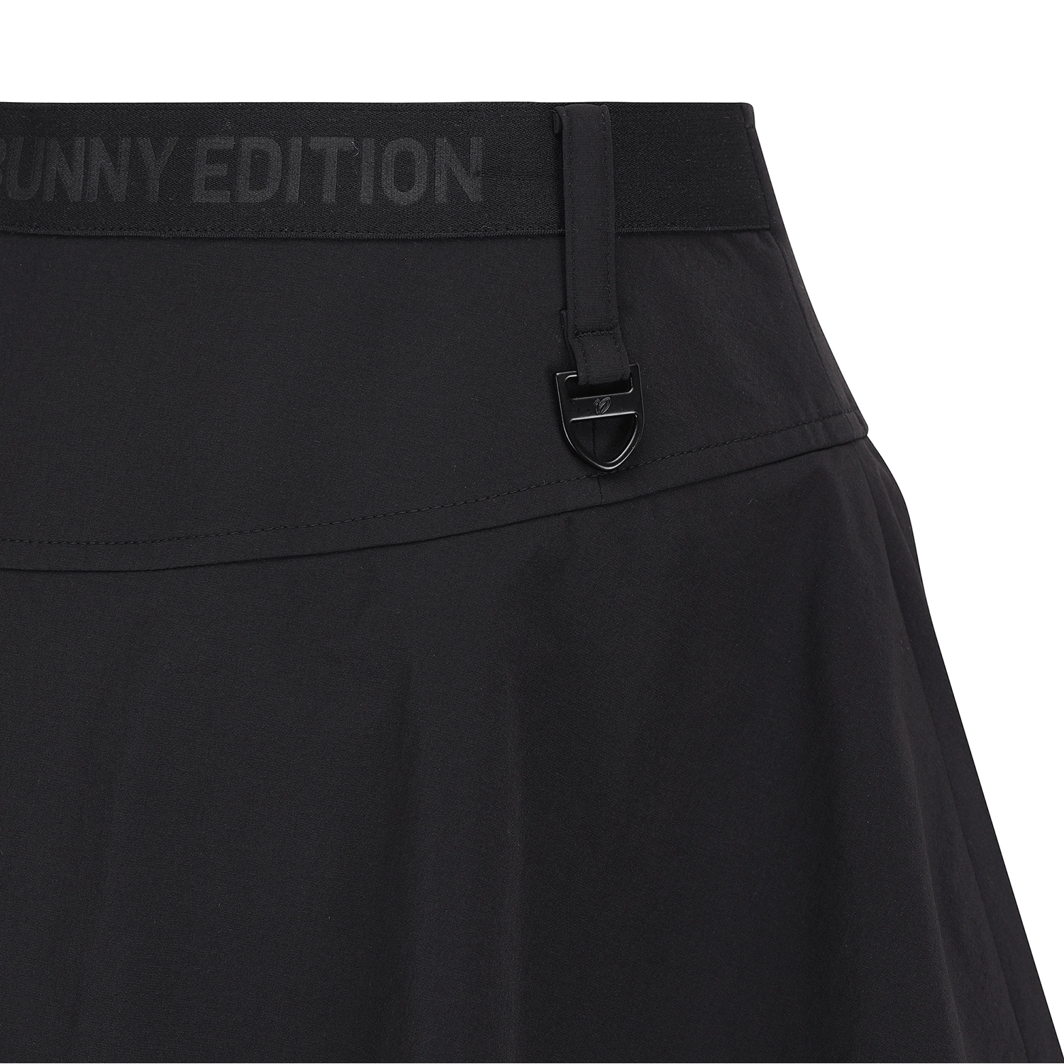 Close-up of a black athletic skirt showing the waistband with 'UNNY EDITION' text and a black metal shield-shaped buckle.