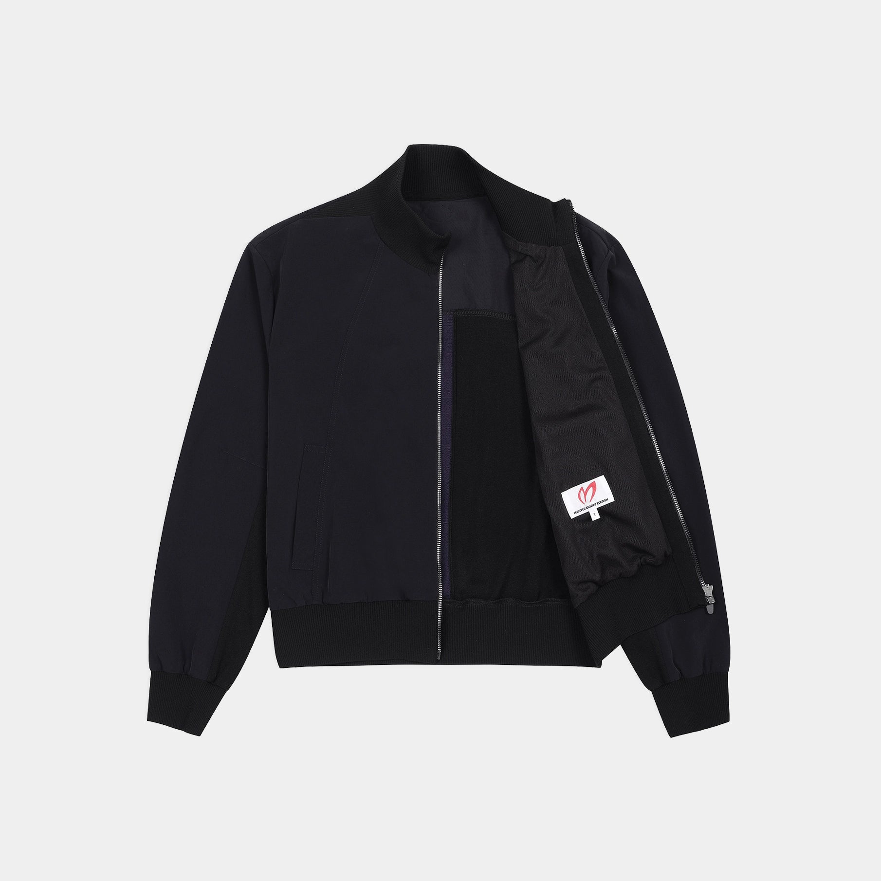A black zip-up bomber jacket with a stand collar, ribbed cuffs and hem, featuring a black interior lining and a small white brand patch on the sleeve.