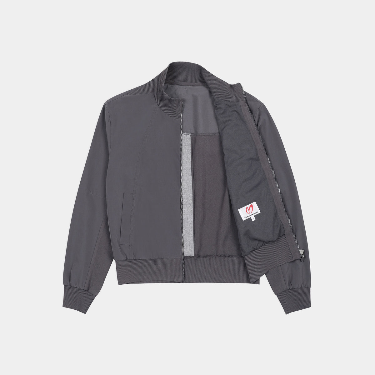 A dark gray zip-up jacket with a high collar, laid flat against a light gray background. The jacket features a vertical lighter gray stripe on the front, a zippered pocket on the left side, and a small white brand patch on the right pocket.