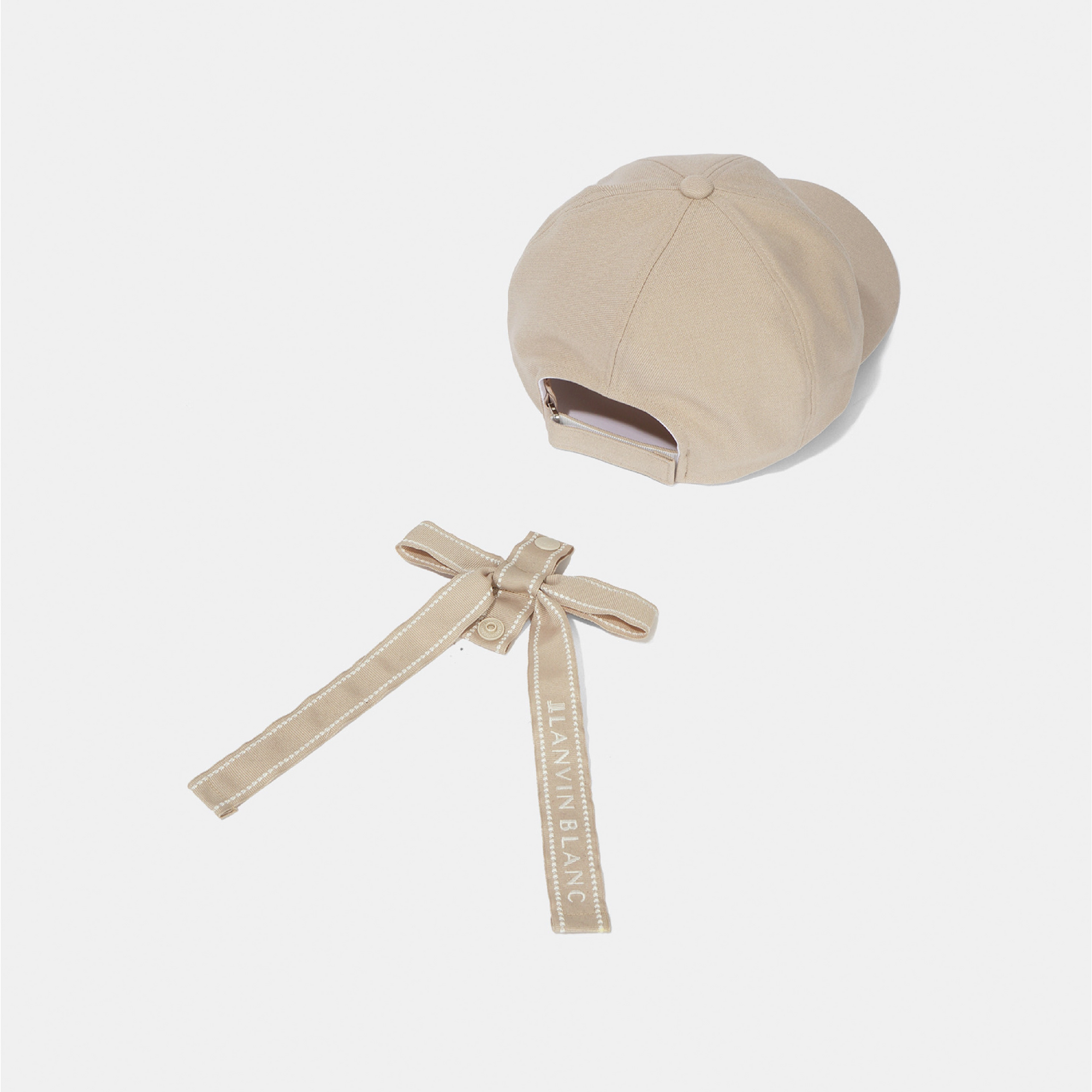 A beige structured baseball cap shown from the back, with a matching fabric tie strap attached and featuring the brand name 'LANVIN-BLANC' printed on it, set against a plain light gray background.