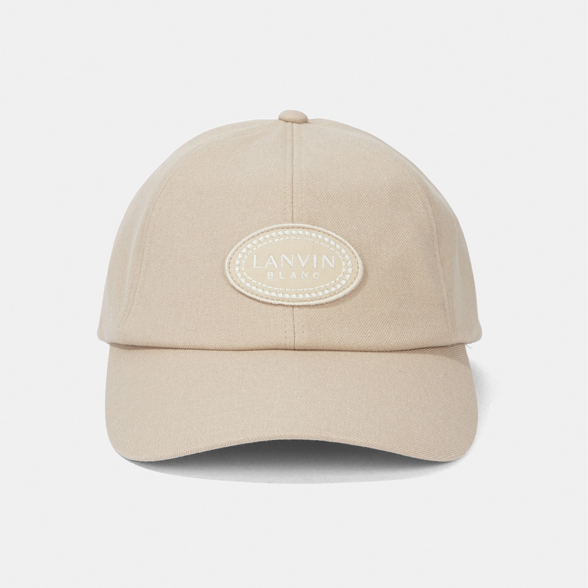 A beige baseball cap with an oval embroidered patch on the front reading 'LANVIN BLANC'.