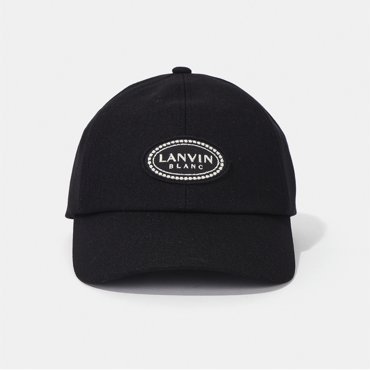 A black baseball cap with an oval embroidered patch on the front that reads 'LANVIN BLANC' in white text surrounded by a dotted border of small rhinestones, photographed on a light gray background.