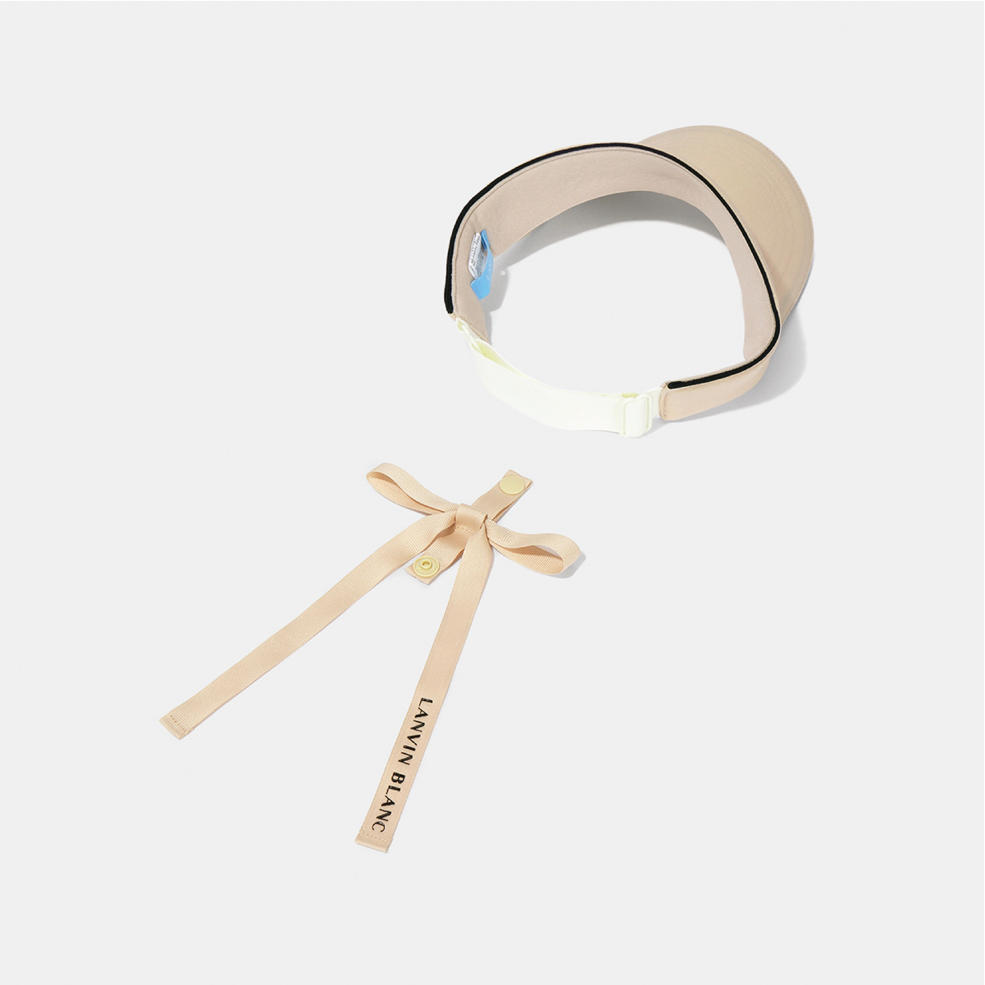 A beige visor-style headband accessory with a matching ribbon tie, photographed on a clean light gray background. The visor has black piping around the edge, a white adjustable strap section, and a long ribbon tail printed with the brand name 'LANVIN BLANC'.