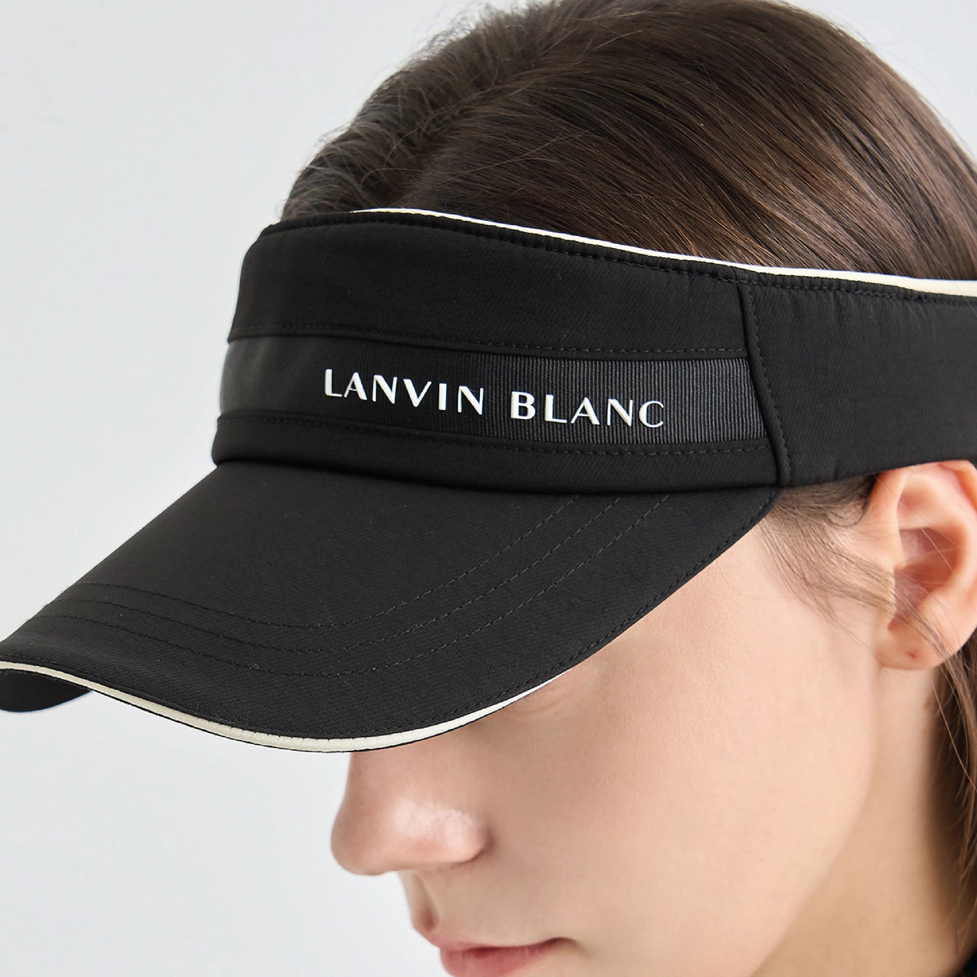 A close-up of a woman wearing a black visor with white trim and the brand name 'LANVIN BLANC' printed on the front band.