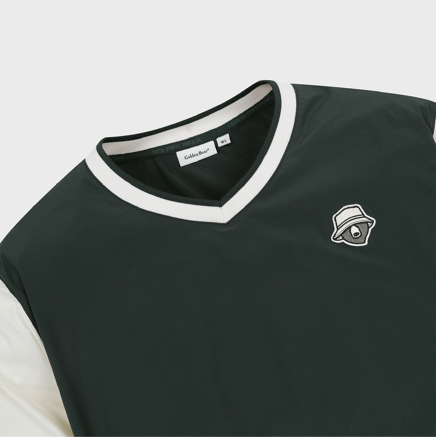 Close-up of a dark forest green V-neck t-shirt with white trim on the collar and sleeves, featuring a small white embroidered logo of a hat-wearing eye on the left chest. The brand name 'Sakurazaki' is visible on the inner neck label.