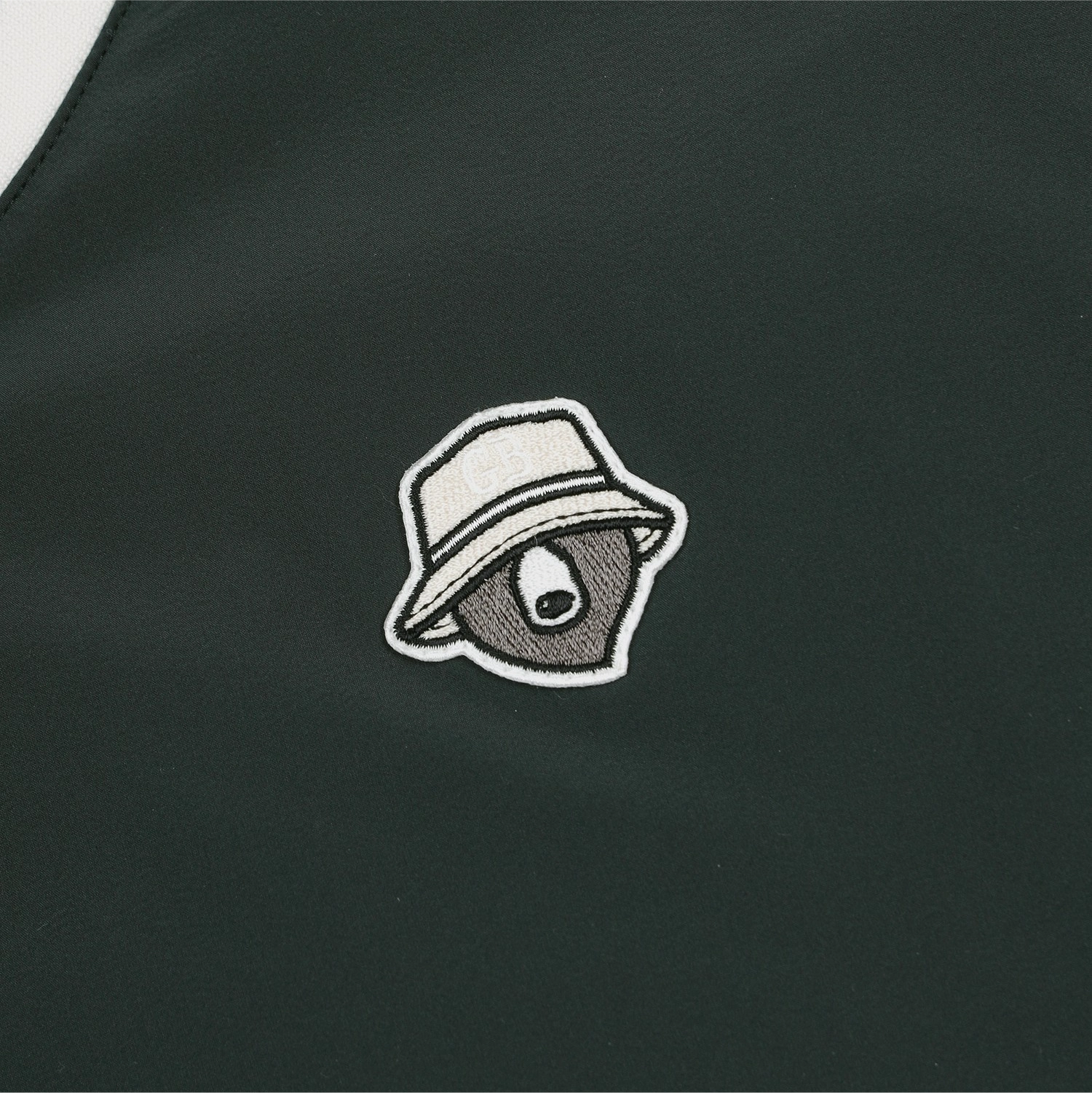Close-up of a dark green garment featuring an embroidered mascot logo of a bear wearing a white bucket hat.