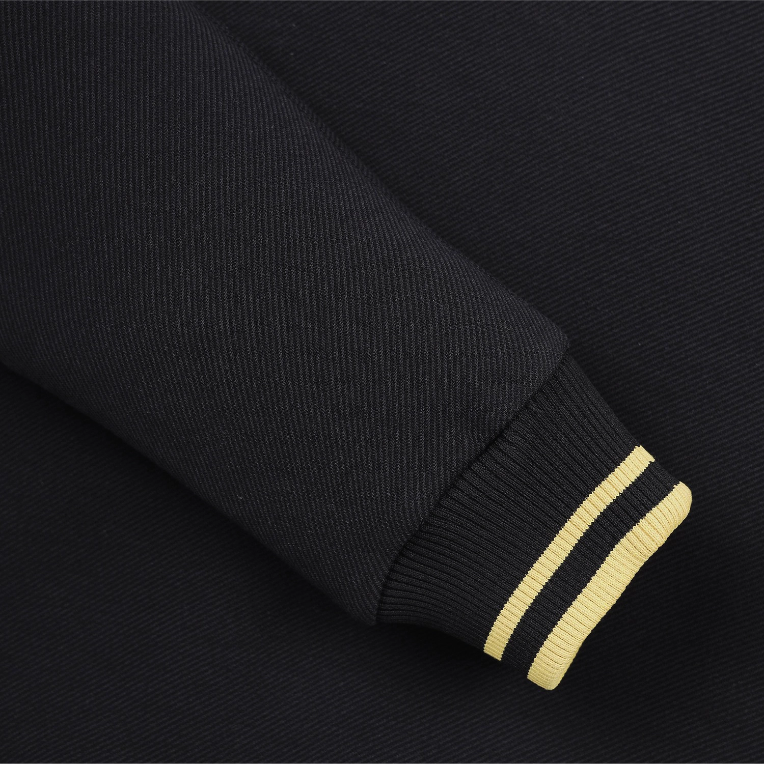 Close-up of a black ribbed knit sleeve cuff with two thin yellow stripes, shown against matching black fabric.