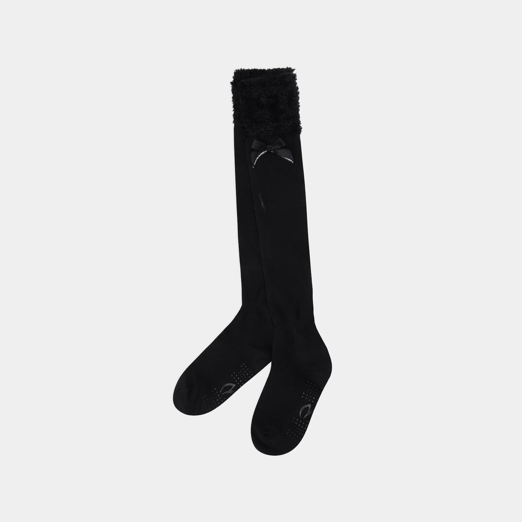 A pair of black over-the-knee socks with a fluffy black faux-fur trim at the top and textured grip dots on the toes, shown against a light gray background.