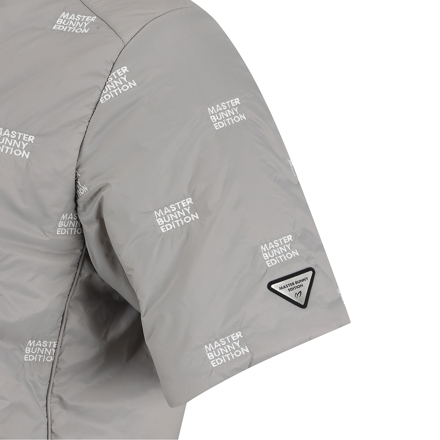 Close-up of a light gray puffer jacket sleeve with an allover repeating 'MASTER BUNNY EDITION' print and a small black triangular patch near the cuff.