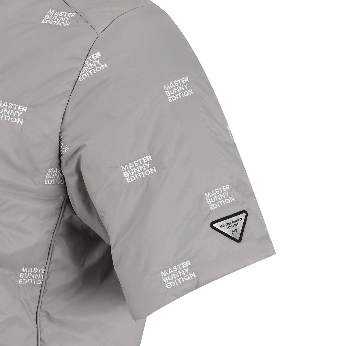 Close-up of a light gray puffer jacket sleeve with an allover repeating 'MASTER BUNNY EDITION' print and a small black triangular patch near the cuff.