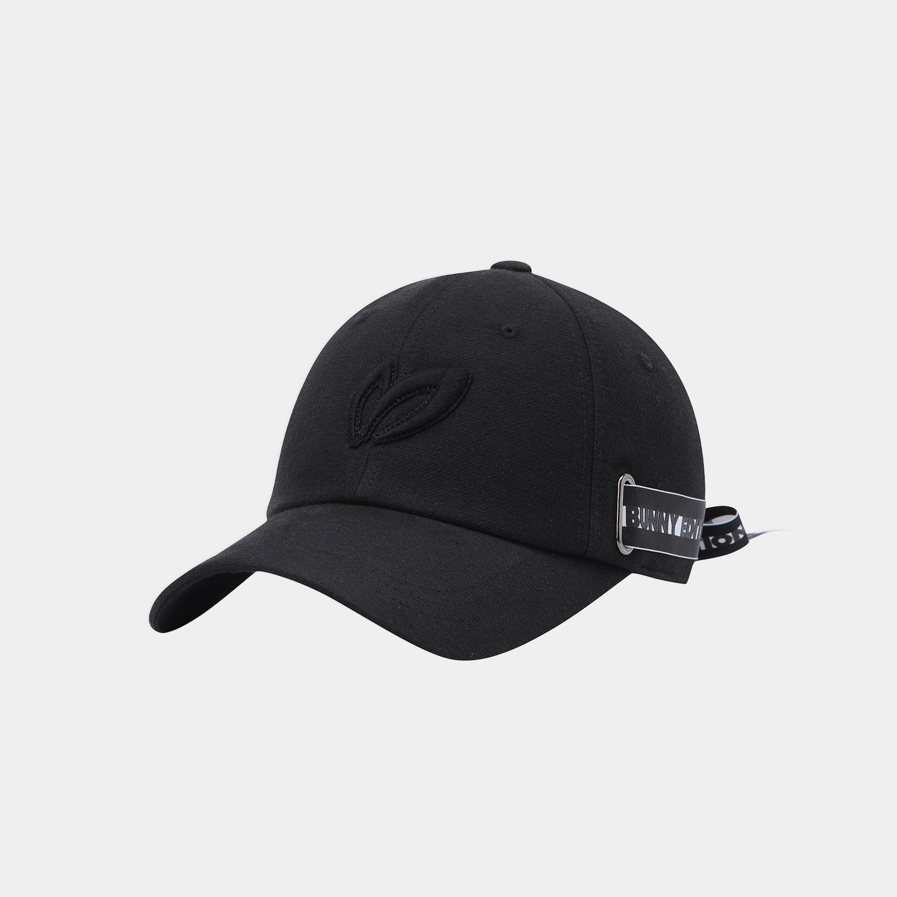 A black baseball cap with a curved brim, featuring a tonal embroidered leaf logo on the front and a small black-and-white brand patch on the side, set against a light gray background.