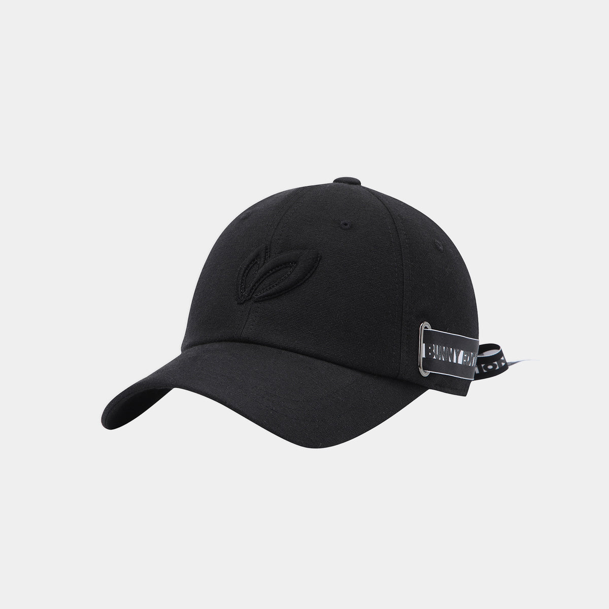 A black baseball cap with a curved brim, featuring a tonal embroidered leaf logo on the front and a small black-and-white brand patch on the side, set against a light gray background.