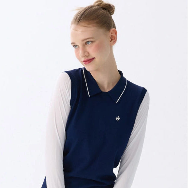 A woman modeling a navy blue sleeveless knit polo vest over a white long-sleeve shirt and white skirt, photographed against a clean white studio background.