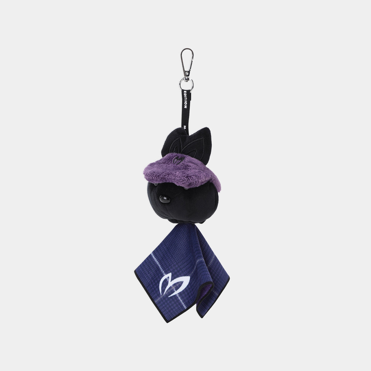 A small plush keychain or bag charm featuring a black cat head with a fuzzy purple hat, attached to a black strap with a metal carabiner, and a navy blue towel with a white cat logo hanging below, shown on a light gray background.