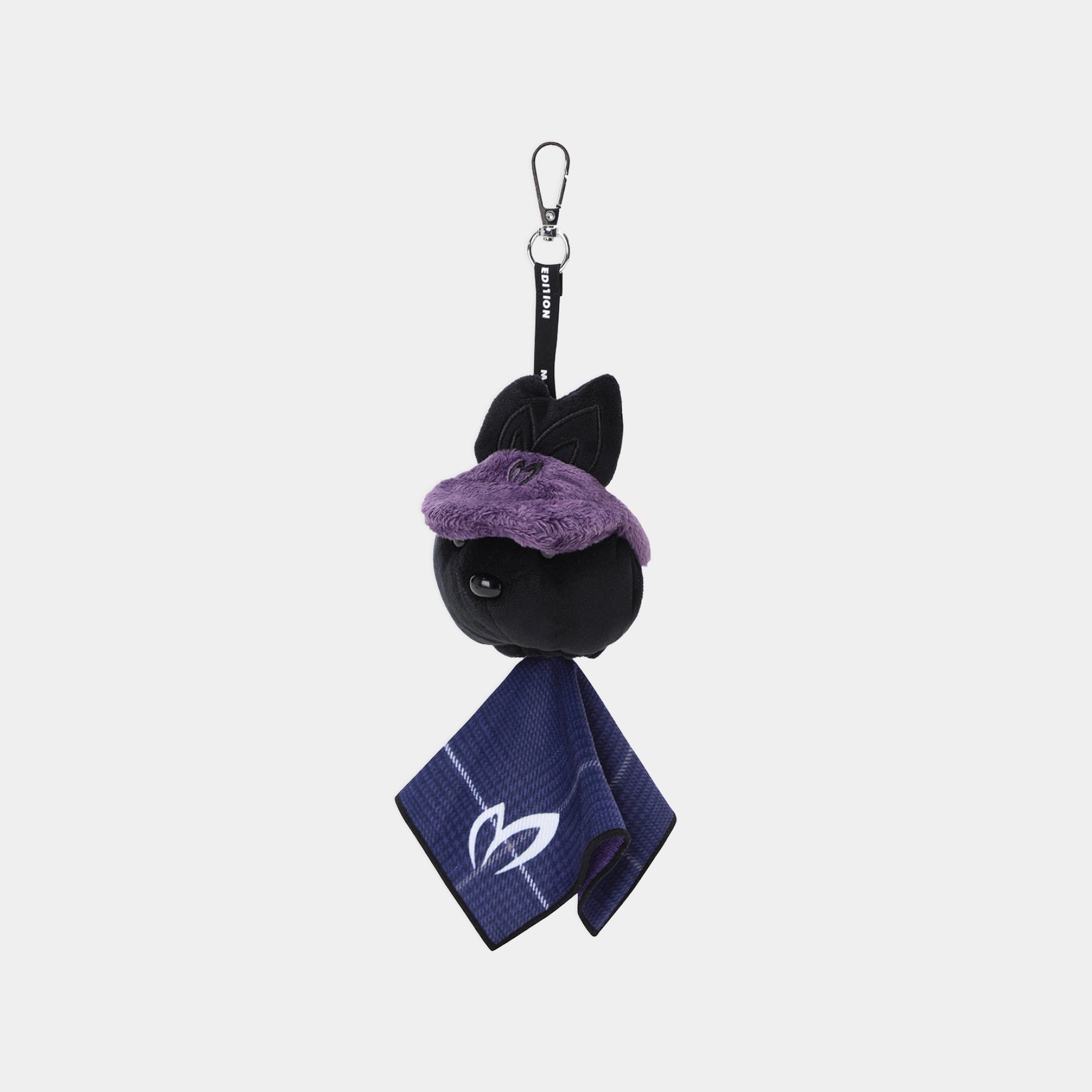 A small plush keychain or bag charm featuring a black cat head with a fuzzy purple hat, attached to a black strap with a metal carabiner, and a navy blue towel with a white cat logo hanging below, shown on a light gray background.