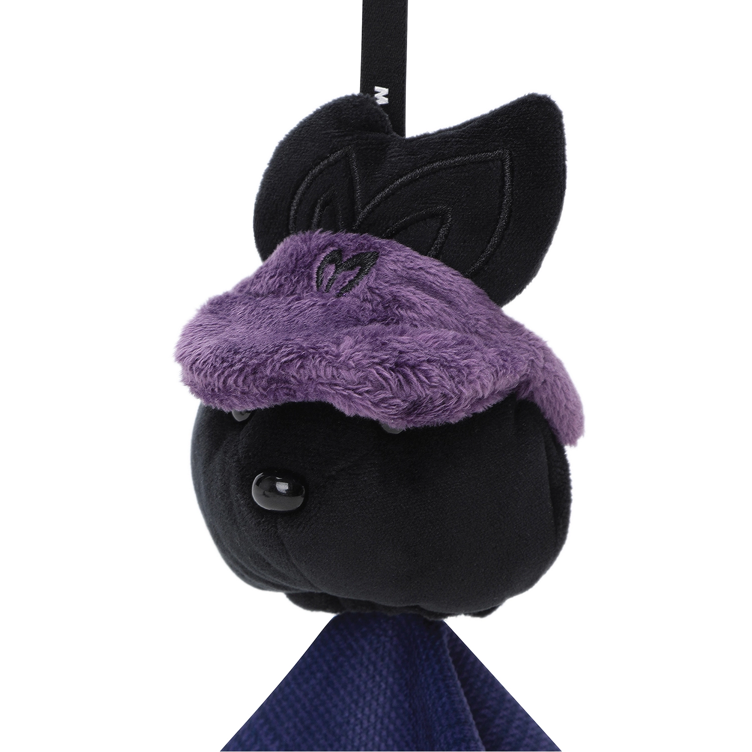 A plush black cat toy or accessory with a fuzzy purple headband, shown against a plain white background. A black strap with a small white letter is visible at the top, and a dark blue fabric hangs below.