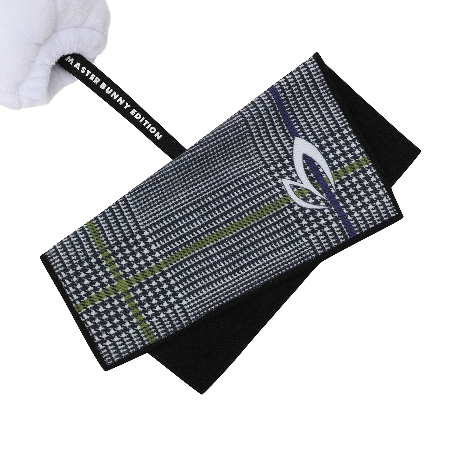 A close-up of a folded black golf towel with a white and gray houndstooth pattern, olive green stripes, and a white club logo. A white gloved hand is holding the black strap on the left, which has white text reading 'MASTER BUNNY EDITION'.