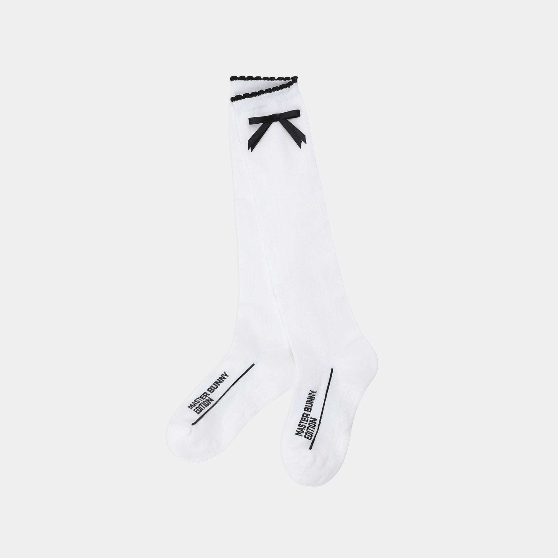 A pair of white knee-high socks with black trim, featuring a black bow at the top and black text branding near the toes, shown against a light gray background.