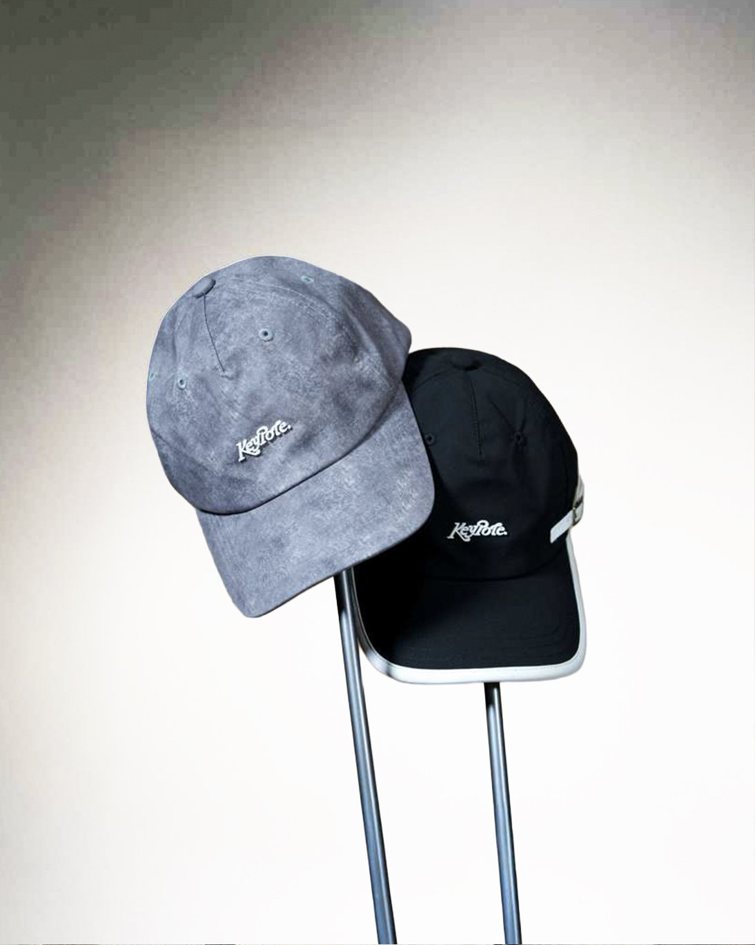 Two baseball caps, one gray and one black, on a stand against a light background.