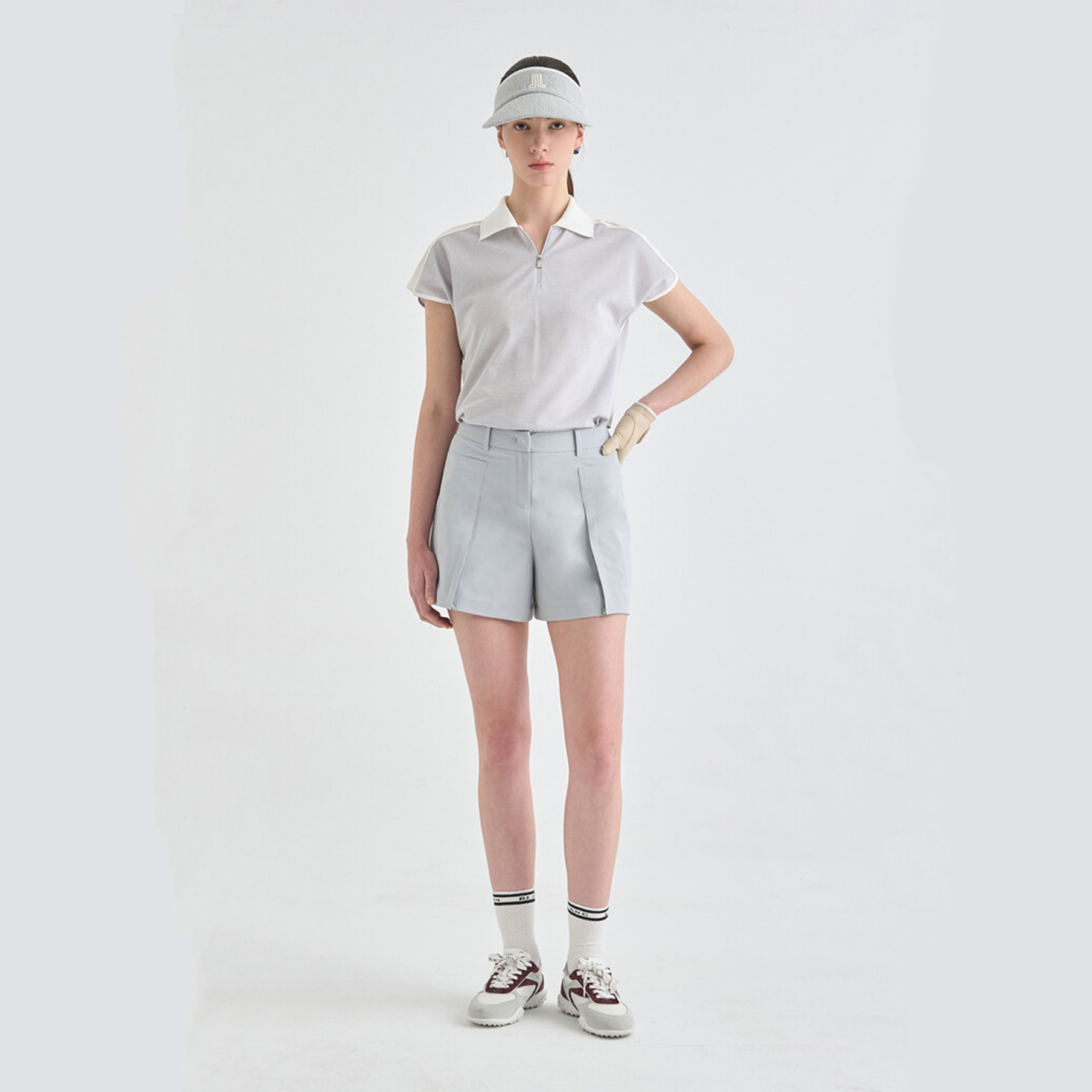Person wearing a white polo shirt, gray shorts, and a visor on a light gray background