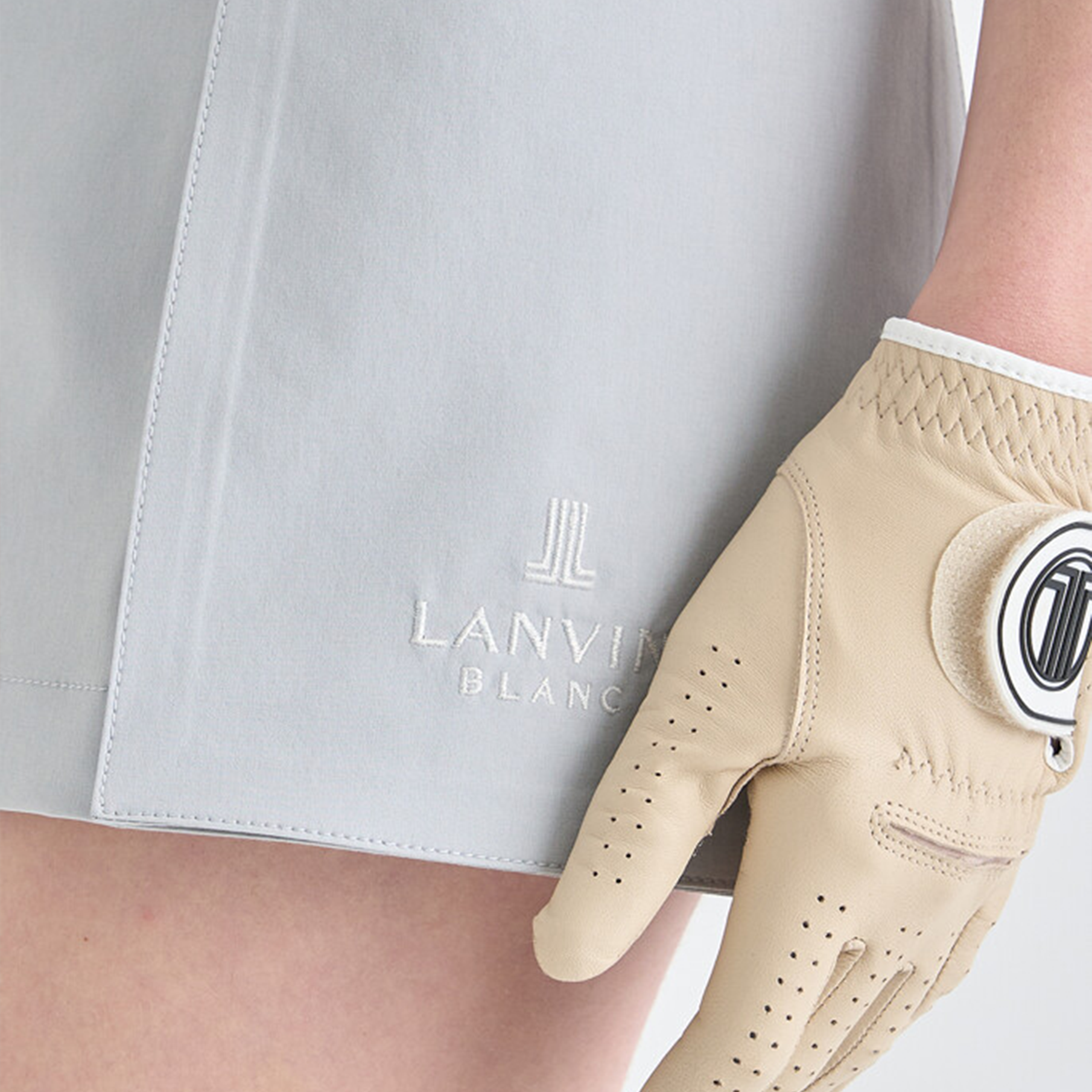 Beige golf glove worn by a person with a gray shorts featuring 'LANVIN' branding.