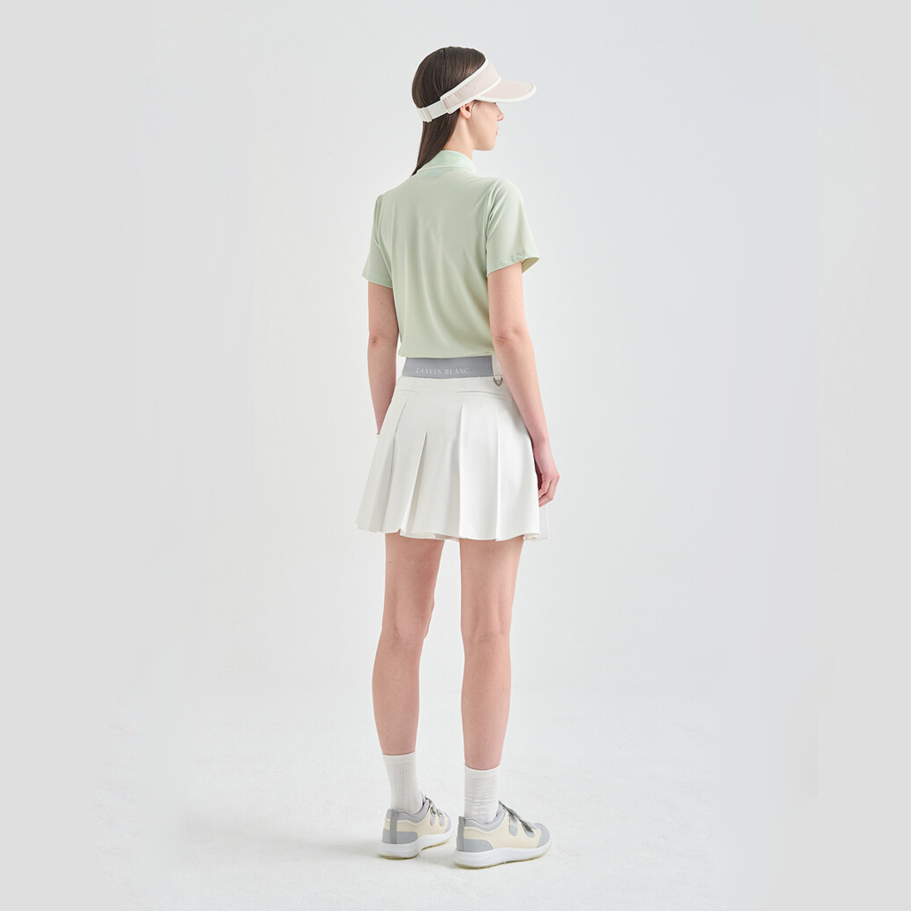 Person wearing a light green polo shirt, white skirt, and gray sneakers on a plain background