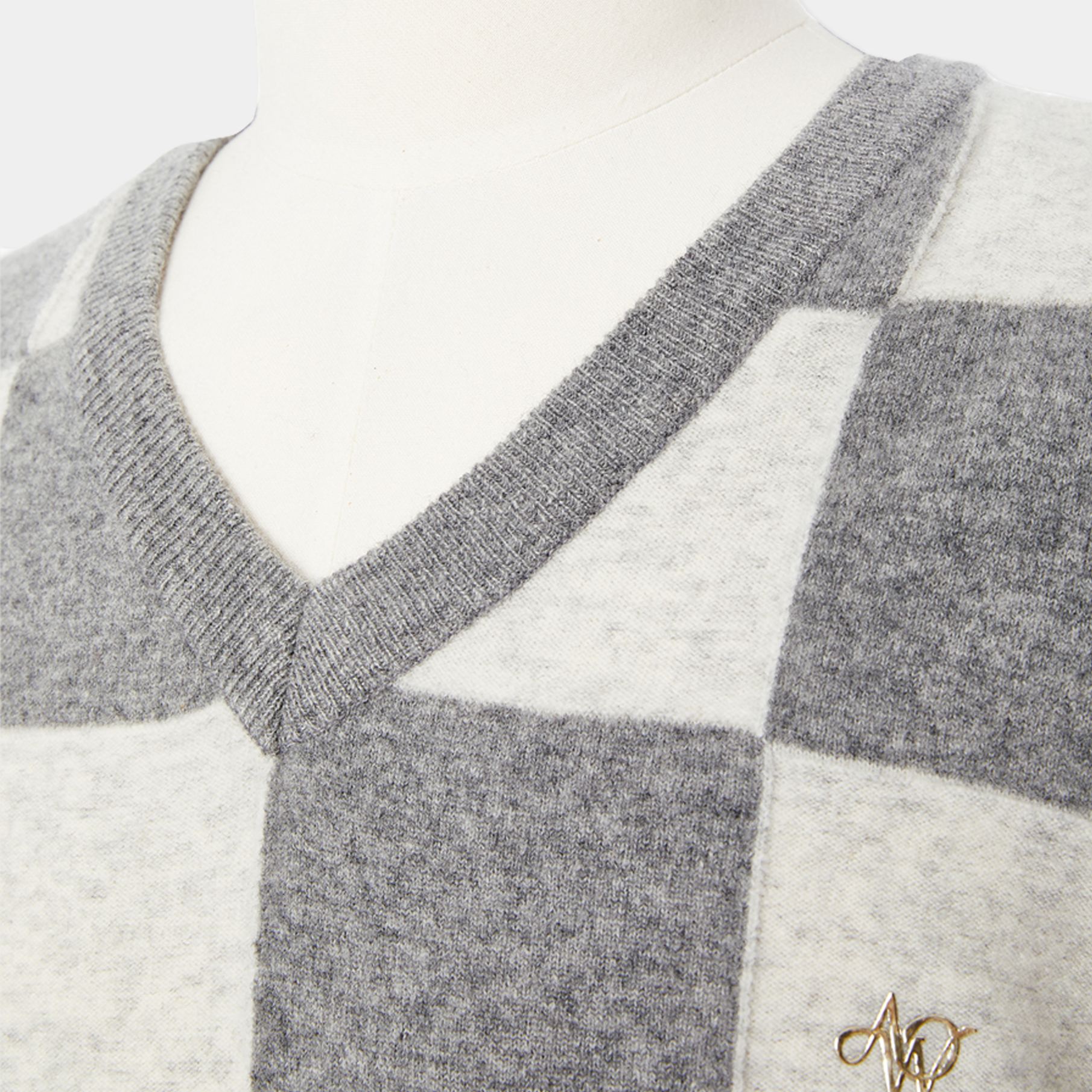Gray and white checkered sweater on a mannequin with a brand logo.